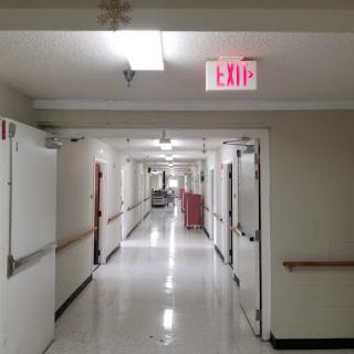 A long, empty hallway in a hospital, featuring exit signs and closed doors.