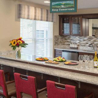 A modern kitchen with a long countertop, red chairs, and decorative elements like flowers and food.