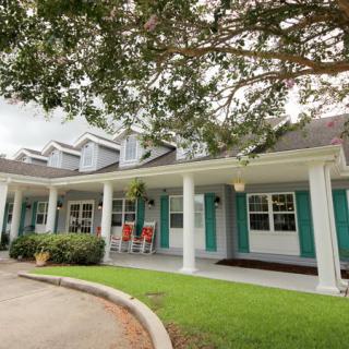 A charming house with a spacious porch and teal shutters set amidst green lawns and trees.