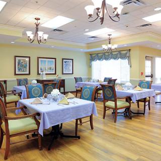 A well-lit dining area with neatly arranged tables and comfortable chairs, featuring elegant chandeliers and hardwood flooring.