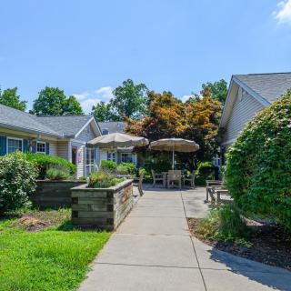 A peaceful outdoor setting with a pathway leading to patio furniture surrounded by lush greenery.