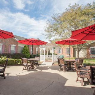 A sunny outdoor patio with tables and red umbrellas in front of a brick building.