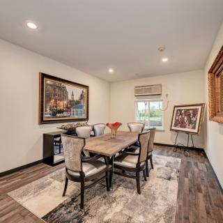 A well-furnished dining room featuring a wooden table with upholstered chairs, artwork on the walls, and a large window allowing natural light to fill the space.