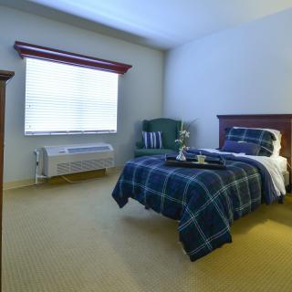 A cozy bedroom with a single bed, armchair, and nightstand by a large window.
