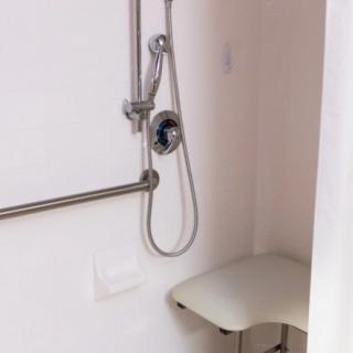 Accessible shower with a handheld showerhead, grab bar, and foldable seat.