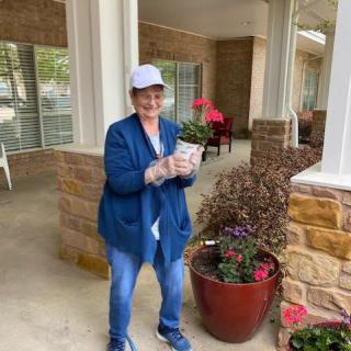 A woman holding a potted plant while smiling outdoors.