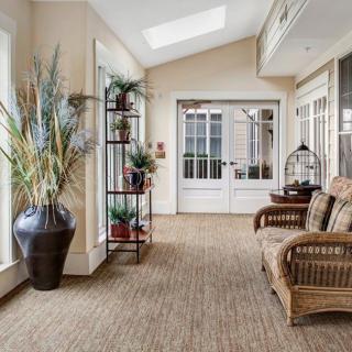 A sunlit conservatory featuring rattan chairs, lush plants, and a skylight.