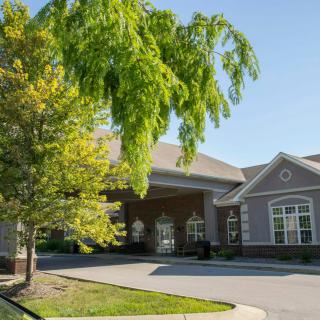 A building with a covered entrance surrounded by trees and a driveway.