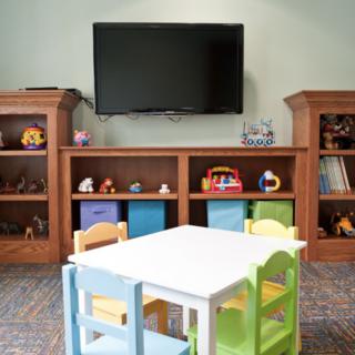 A cozy children's playroom with a small table and colorful chairs, surrounded by bookshelves filled with toys.