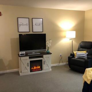 Cozy living room with a television set atop a fireplace, an armchair, and warm lighting.