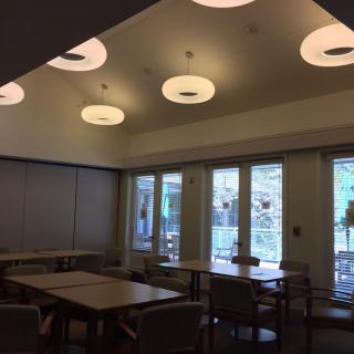 A well-lit dining area with tables and chairs, featuring large windows and modern lighting fixtures.