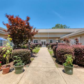 A sunny day view of a building with a garden pathway lined with plants and bushes.