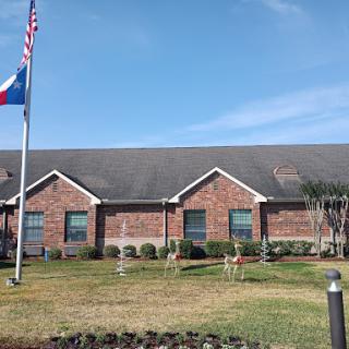A brick building featuring the Texas flag, surrounded by well-maintained landscaping under a clear blue sky.