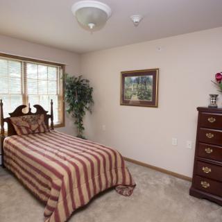 A cozy bedroom with a single bed, dresser, and large window.