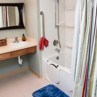 An accessible bathroom with a bathtub, grab bars, and a striped shower curtain.