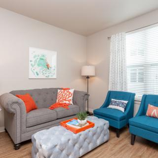 A cozy living room with a gray sofa, two blue armchairs, and bright orange accents.