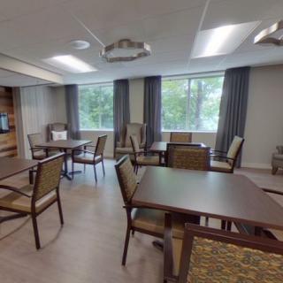 A dining area with multiple tables and chairs, featuring large windows with curtains.