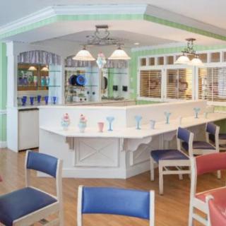 A bright and inviting cafe interior with a central counter surrounded by colorful chairs.