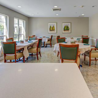 A bright and spacious dining room with neatly arranged tables and chairs, featuring large windows and wall artwork.