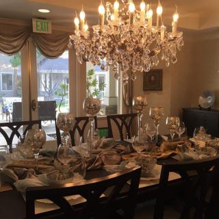 An elegantly set dining room with a sparkling chandelier and neatly arranged table settings.