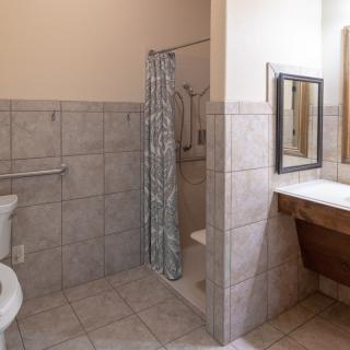 A well-lit bathroom with a shower, toilet, and sink, featuring tiled walls and flooring.