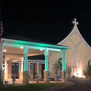 A church building illuminated at night with a prominent cross on its steeple.
