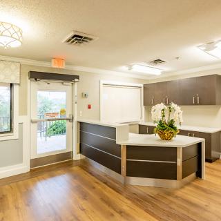 A modern reception area with wood flooring and a central counter desk, featuring contemporary lighting.