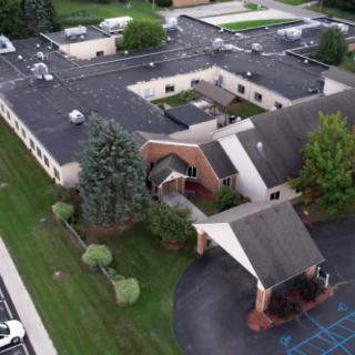 Aerial view of a building with surrounding greenery and a parking area.