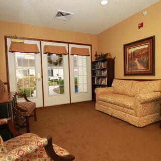 A cozy living room with a sofa, armchair, bookshelf, and glass doors leading outside.