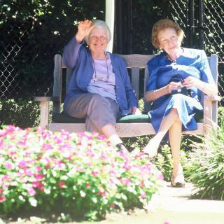 Two elderly women sitting on a bench, enjoying a sunny day in the garden.