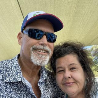 A couple taking a selfie outdoors under a shaded area.