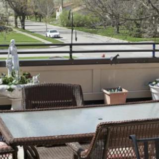 A cozy outdoor patio with a table and chairs, adorned with potted plants, overlooking a street.
