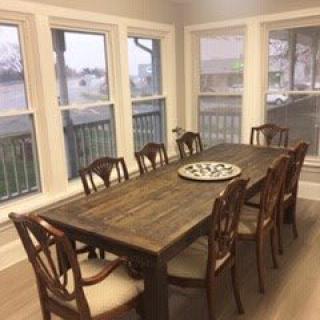 A bright dining room with a large wooden table and several chairs, surrounded by windows.