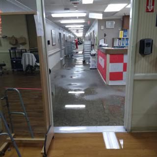 A view of a hospital hallway with wet floors, likely undergoing cleaning.