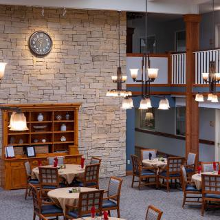 A cozy restaurant dining area with round tables, wooden chairs, a stone wall, and elegant chandeliers.