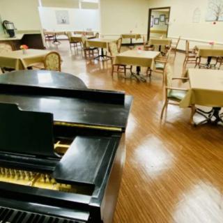 A spacious dining area with a piano and neatly arranged tables and chairs.
