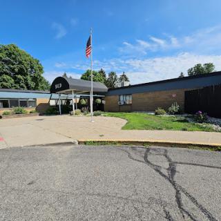 A sunny day at the school entrance, featuring a flag and well-maintained landscaping.