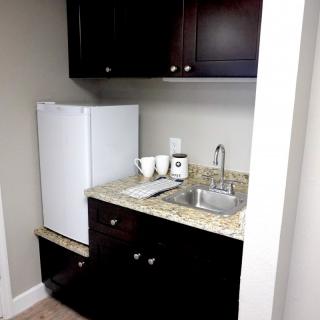 A compact kitchenette with a mini fridge, sink, and coffee setup.