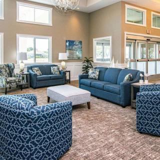 A spacious and well-lit living room featuring blue sofas, patterned armchairs, a central coffee table, and stylish decor.