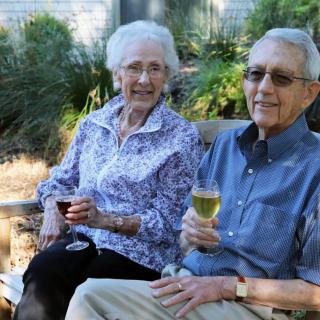 An elderly couple enjoying wine while sitting outdoors in a garden.