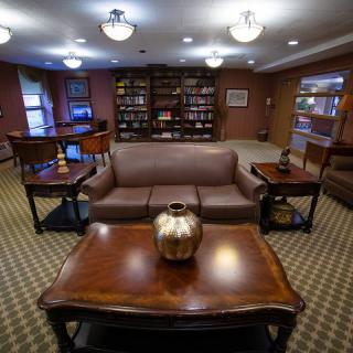 A cozy library reading room featuring bookshelves, a sofa, and wooden tables with decor.
