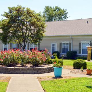 A landscaped garden in front of a single-story building with a tree and flowers.
