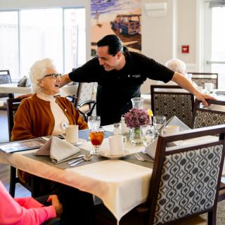 A man engages in a friendly conversation with an elderly woman in a dining area.