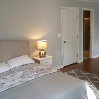 A cozy bedroom featuring a neatly made bed, a nightstand with a lamp, and an open door leading to another room.