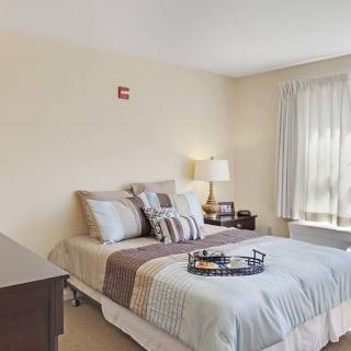 A cozy bedroom with a neatly made bed, pillows, and a bedside lamp near a window with curtains.