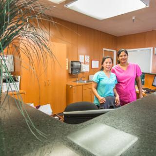 Two staff members pose at a reception desk in a healthcare setting.