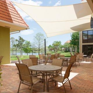 A serene outdoor patio with tables, chairs, and shade sails overlooking a garden area.