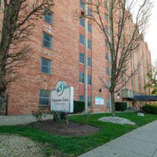 A brick residential apartment building with a sign in the foreground and trees along the sidewalk.