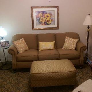 A cozy living room setup with a sofa, ottoman, and a floor lamp, decorated with floral wall art.