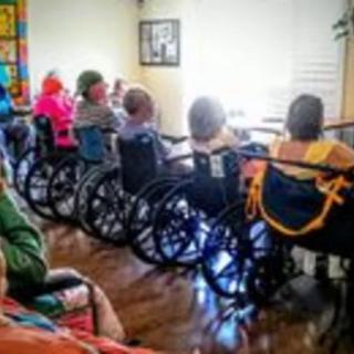 A group of elderly individuals seated in wheelchairs, gathered indoors at a nursing home.